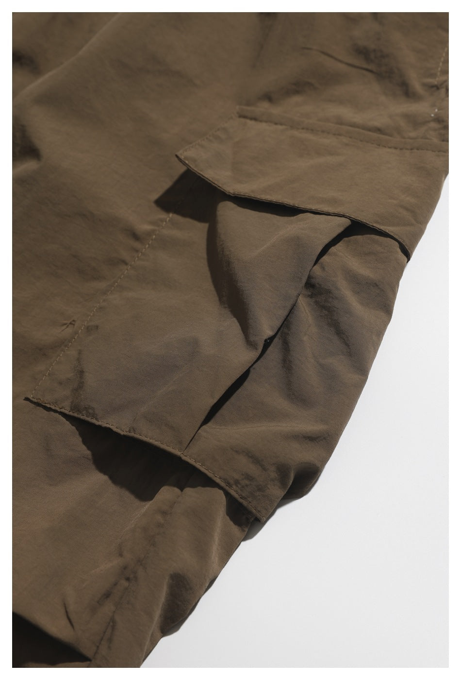 Close-up of a brown shorts pocket flap and stitched seams on a white background.
