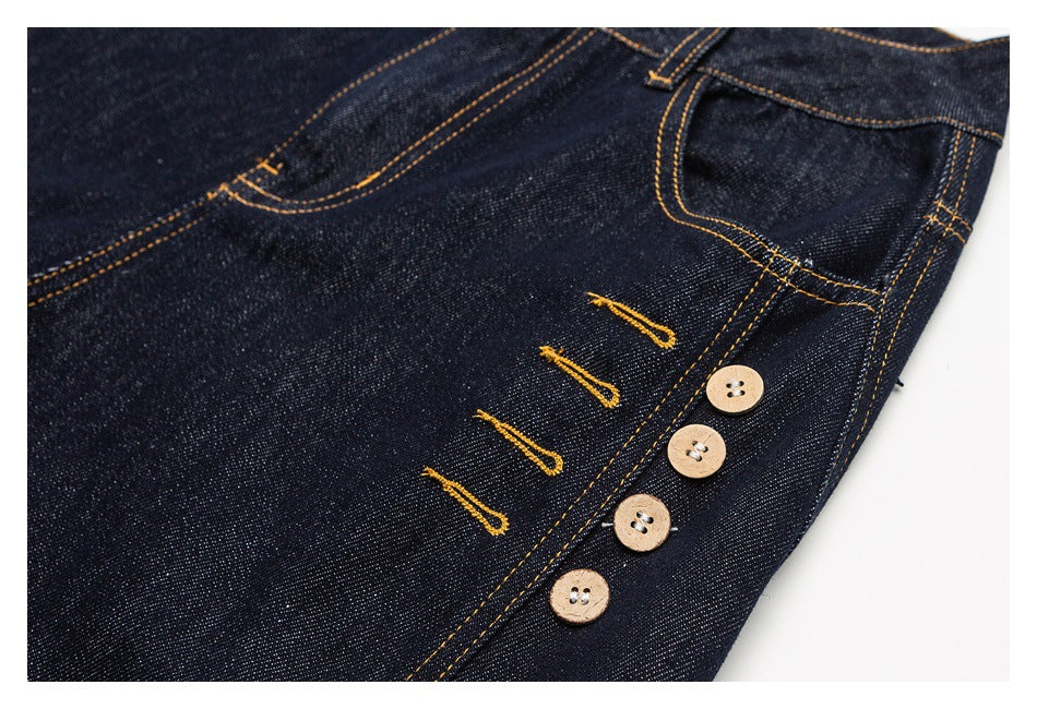 Close-up of dark indigo jeans showing a four-button fly and golden contrast stitching.