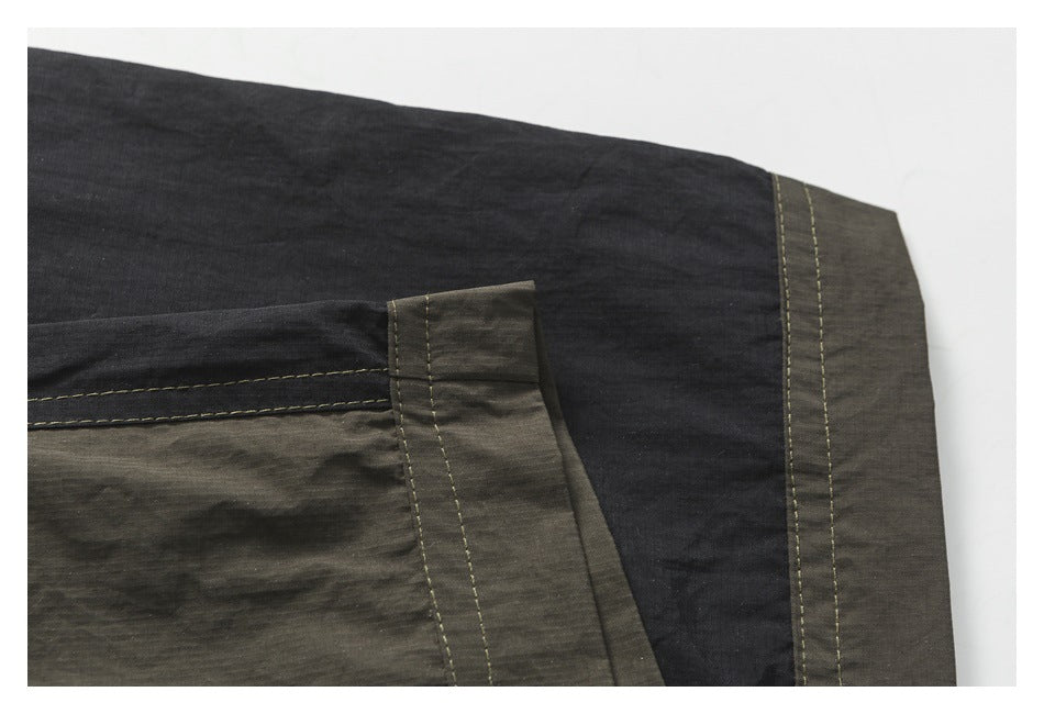 Close-up of dark garment panels with olive-gray trim and parallel contrast-stitched seams.