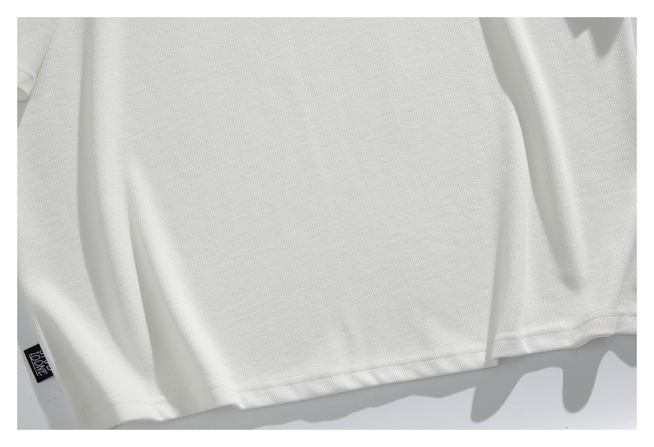 Close-up of the white top's plain body and stitched hem, with a small black sewn-in label at the edge.