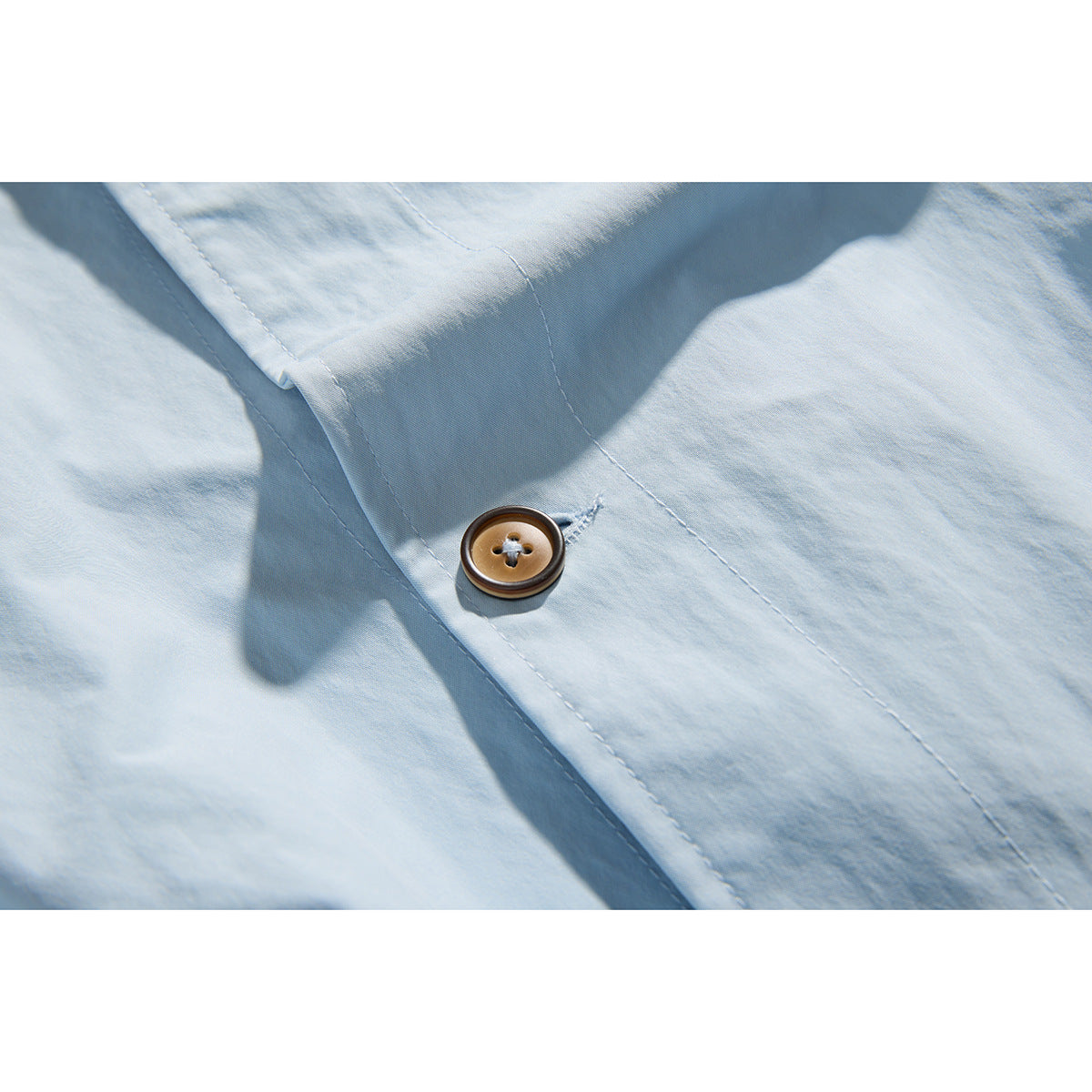 Close-up of a brown button and stitching on the placket of a light blue shirt.