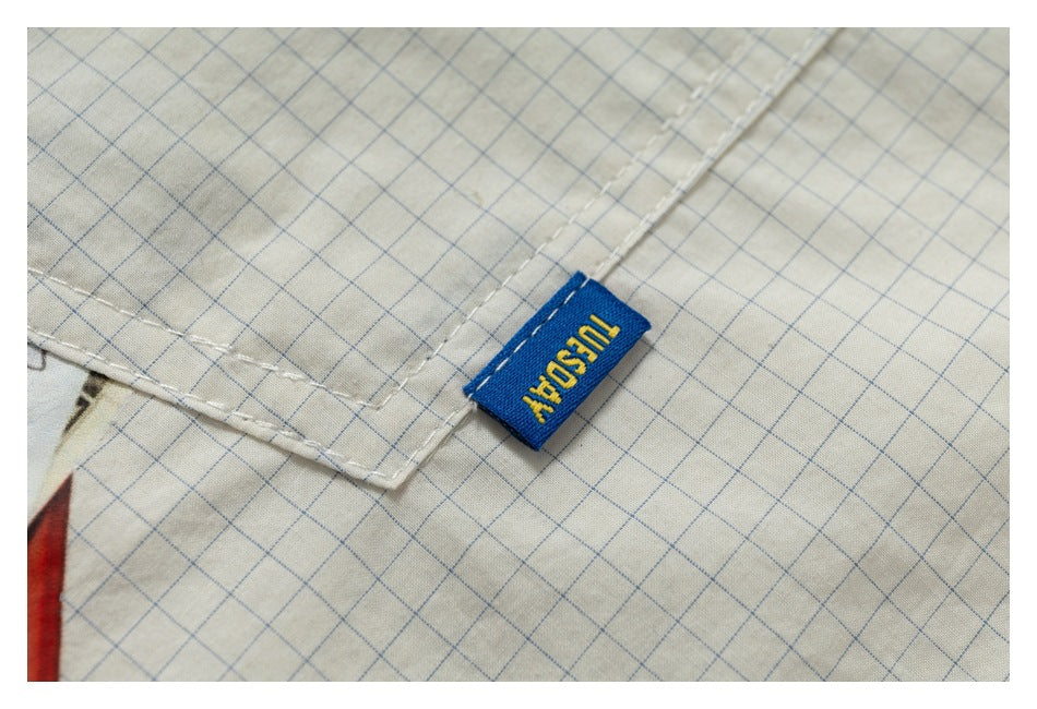 Close-up of cream fabric with a fine blue grid, white stitching, and a small blue woven tab.