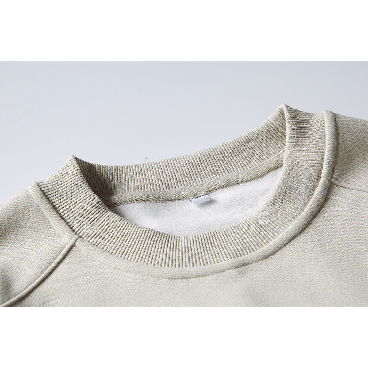 Close-up of a light beige sweatshirt's ribbed crew neck and soft white inner lining.