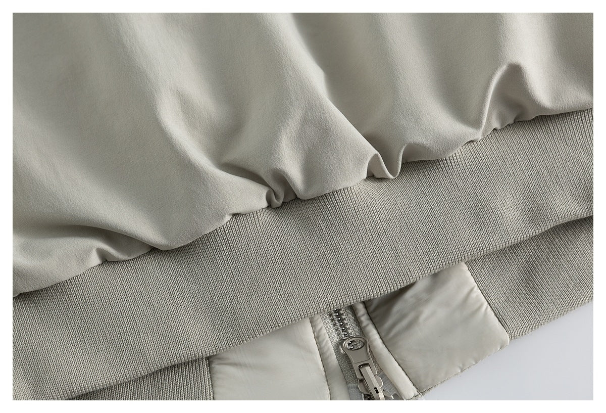 Close-up of a light gray garment with a ribbed band, zipper, and smooth panels.
