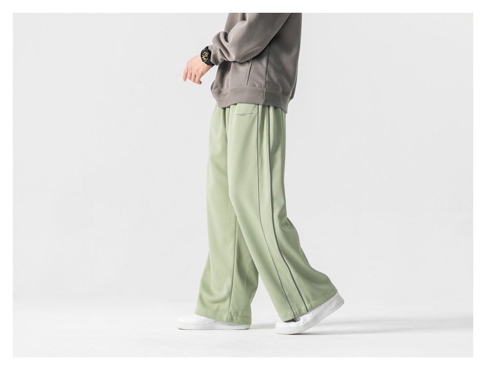 Side view of a model walking in pale sage-green wide-leg pants with a gray hoodie and white sneakers.