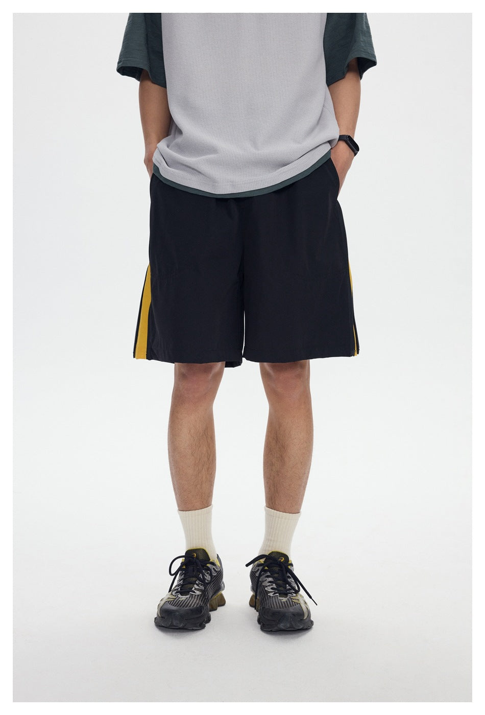 Close view of black shorts with yellow side inserts, worn with a light gray and dark green T-shirt.