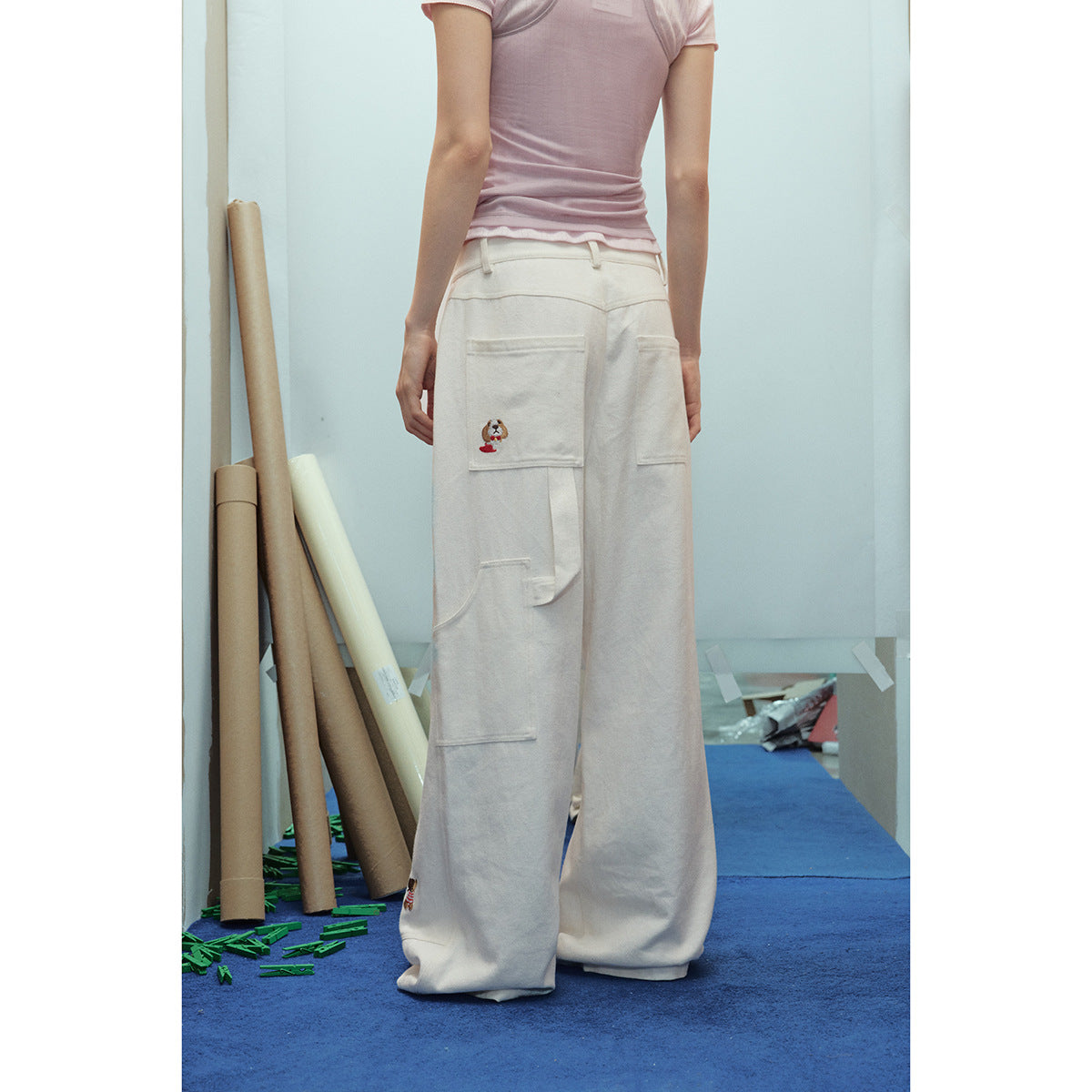 Back view of a model wearing ivory wide-leg cargo pants with large pockets and a small embroidered character.