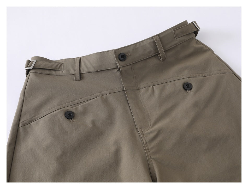 Close-up of taupe shorts showing the waistband, side adjusters, button closure, and pocket details.