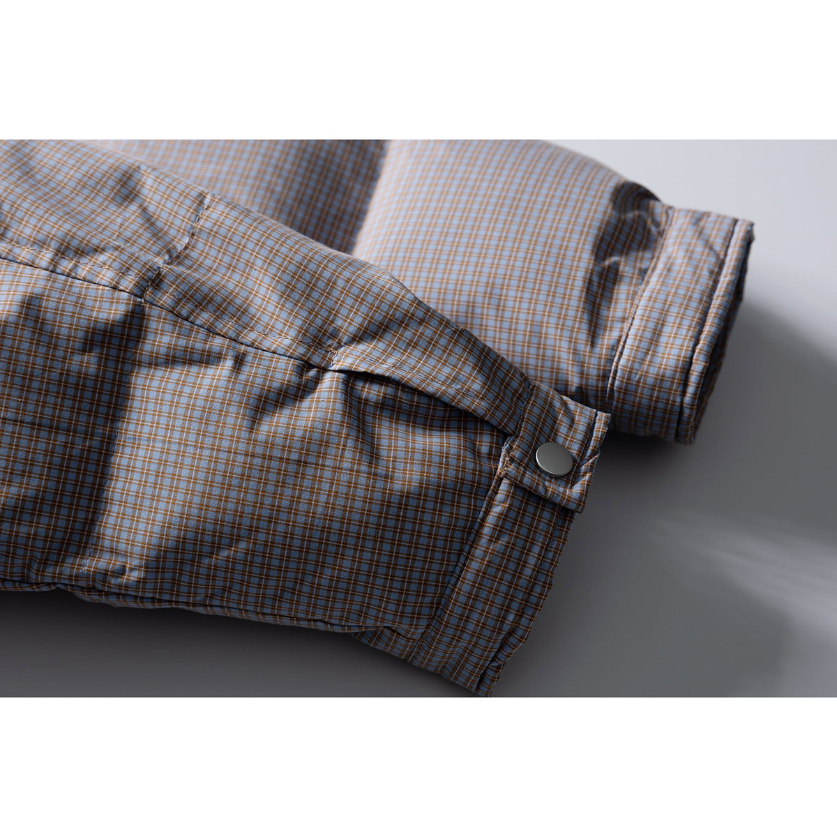 Close-up of the checked jacket sleeve cuff, snap-button tab, and padded body.