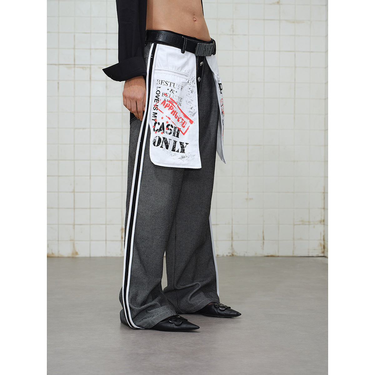 Side view of a model wearing wide gray trousers with white text-print panels and white side stripes.