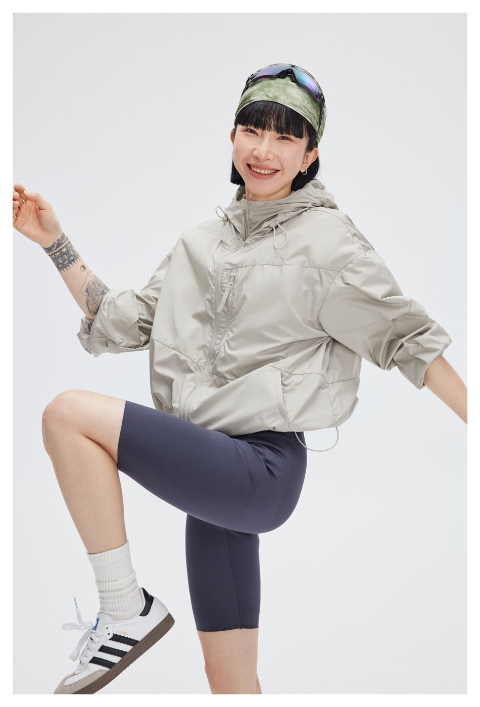 Model wearing a light gray hooded jacket and navy cycling shorts, posed with one knee raised.