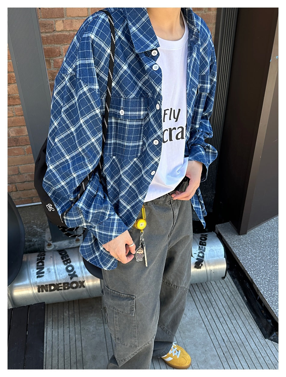 Person wearing the blue plaid shirt open over a white graphic tee with gray cargo pants, cropped torso view