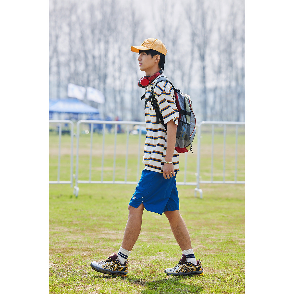 Man walking outdoors in a white multicolor striped pocket T-shirt and bright blue shorts.