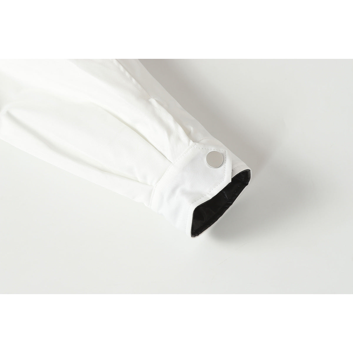Close-up of a white jacket sleeve cuff with a silver snap and black lining.