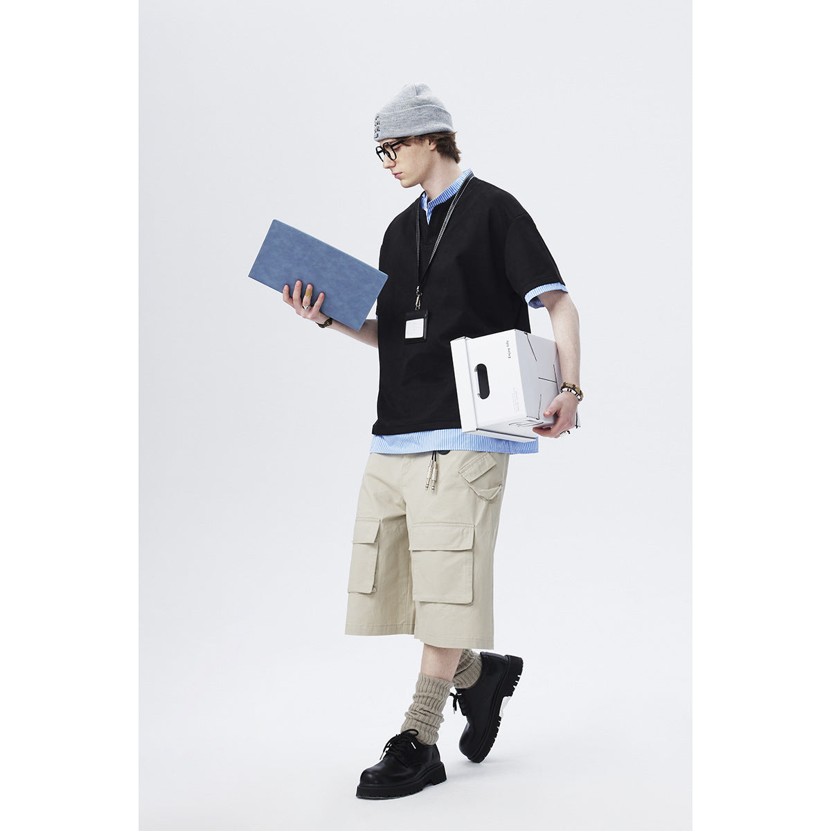 Full-length model wearing an oversized black top with blue striped trim and beige cargo shorts.