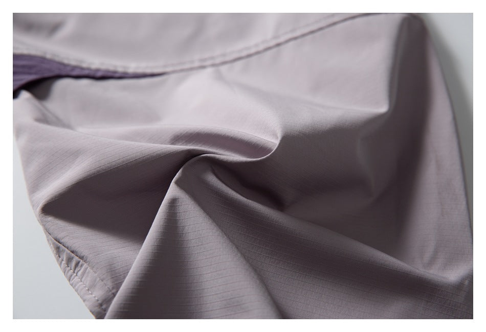 Close-up of pale mauve trouser fabric showing fine grid texture, folds, and stitching.