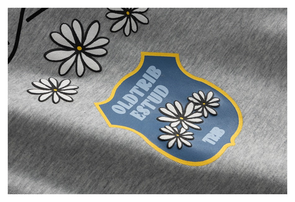 Close-up of a blue shield graphic with yellow edging, white lettering, and daisies on gray fabric.