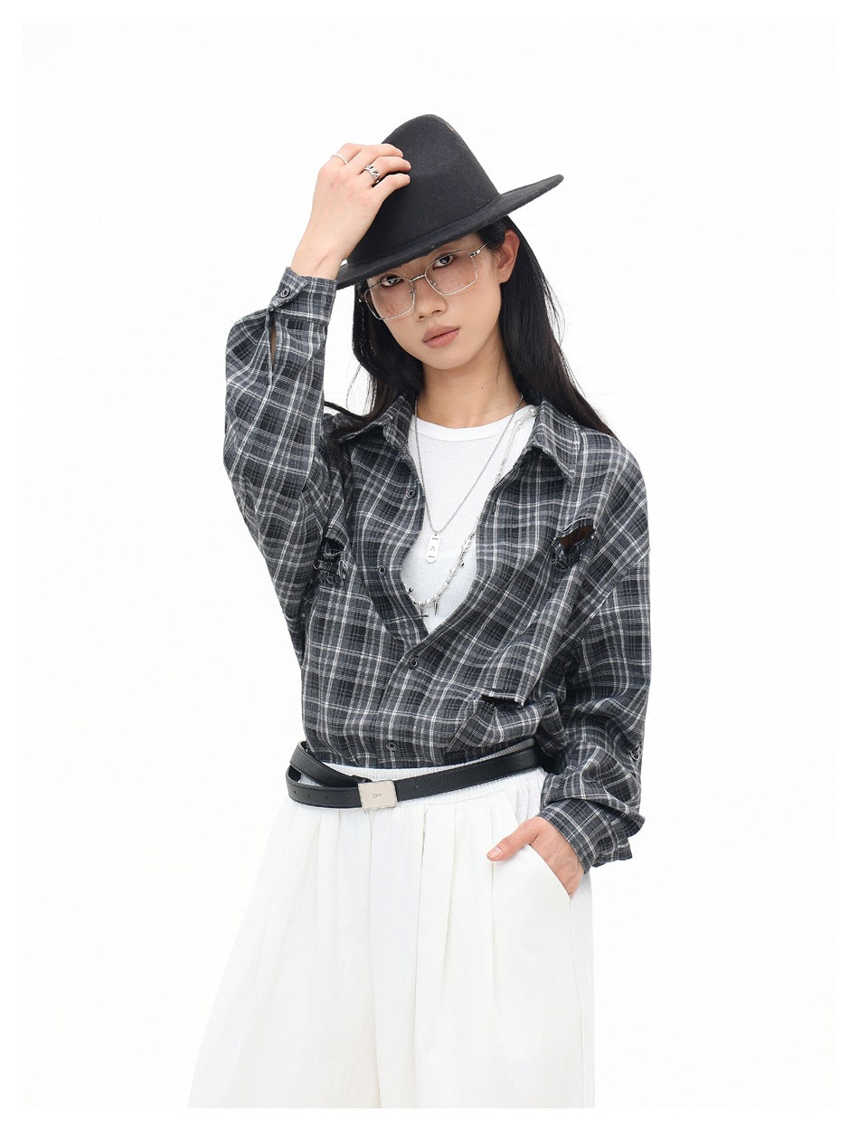 Model wearing an open charcoal gray plaid shirt over a white top, with wide white trousers, a black hat, and belt.