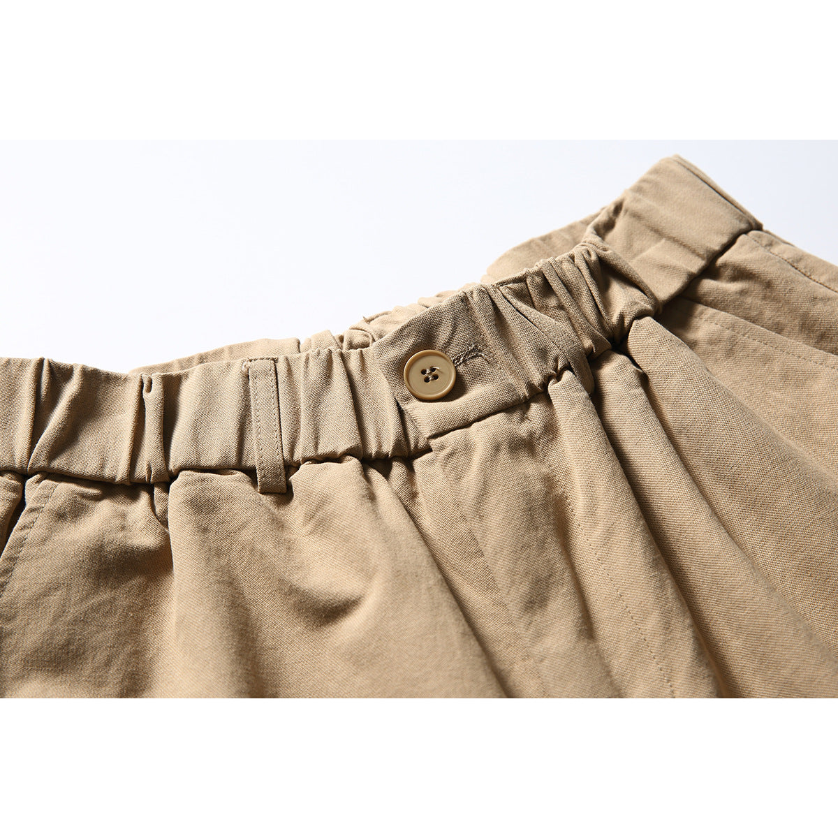 Close-up of tan cargo shorts showing the gathered waistband, belt loop and button.