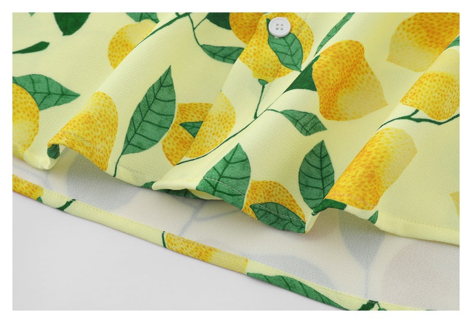 Close-up of the lemon-and-leaf print and stitched hem on a pale yellow shirt, with one white button visible.
