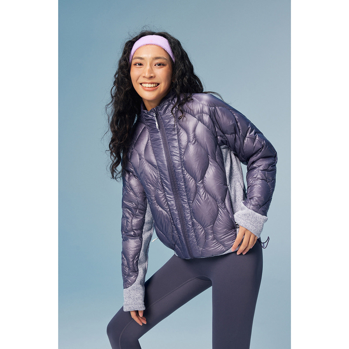 A model wears a purple quilted zip jacket with gray contrasting sleeves and cuffs.
