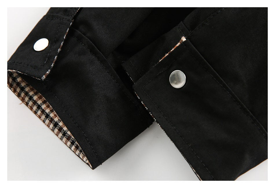 Close-up of two silver snap fasteners and brown, cream, and black checked lining on a black garment.