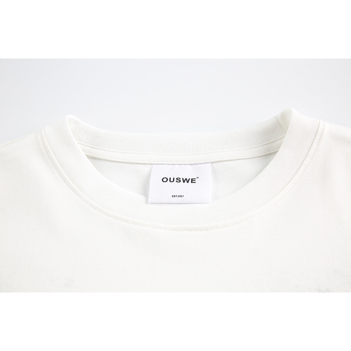 Close-up of an off-white crew-neck T-shirt collar and sewn OUSWE label.
