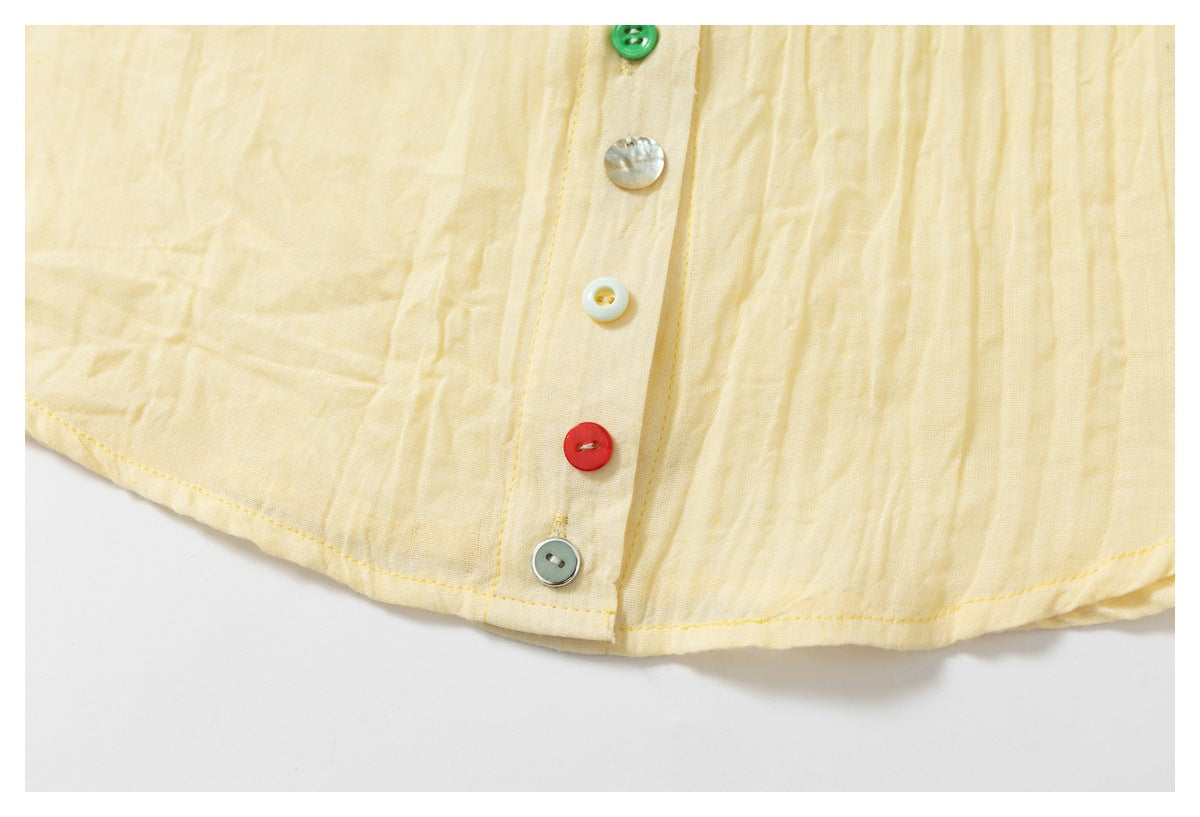 Close-up of the pale yellow shirt's lower placket, colorful buttons, curved hem, and stitching.