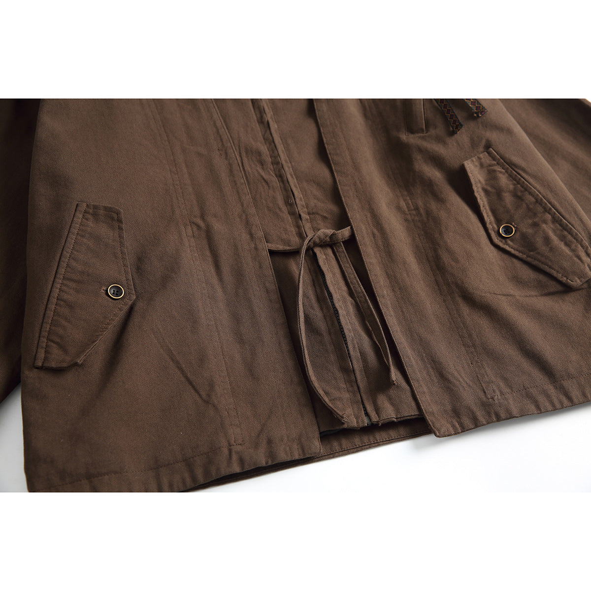 Close-up of the brown jacket’s lower front, showing buttoned flap pockets and a hanging waist tie.