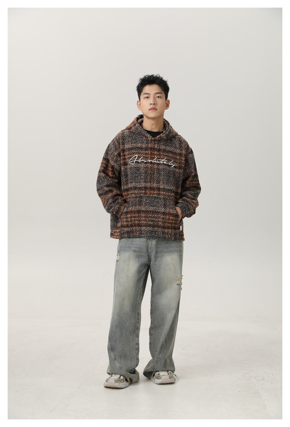 Full-length front view of a man wearing a striped hooded pullover with white chest script, loose gray jeans and sneakers.