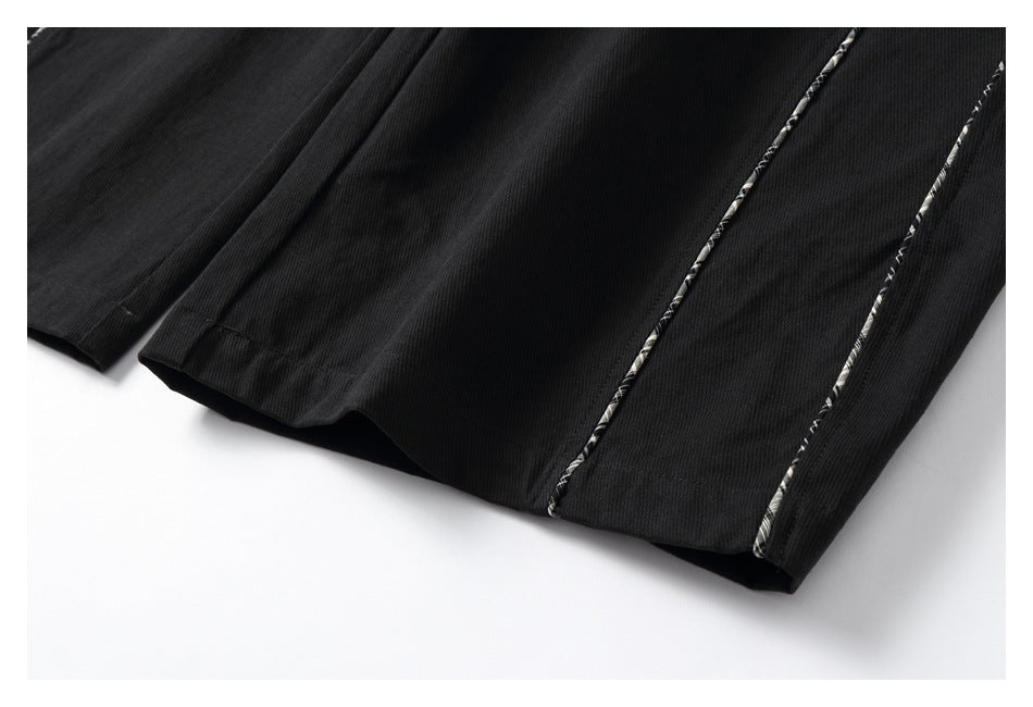 Close-up of black trouser hems showing straight stitching and narrow plaid piping.
