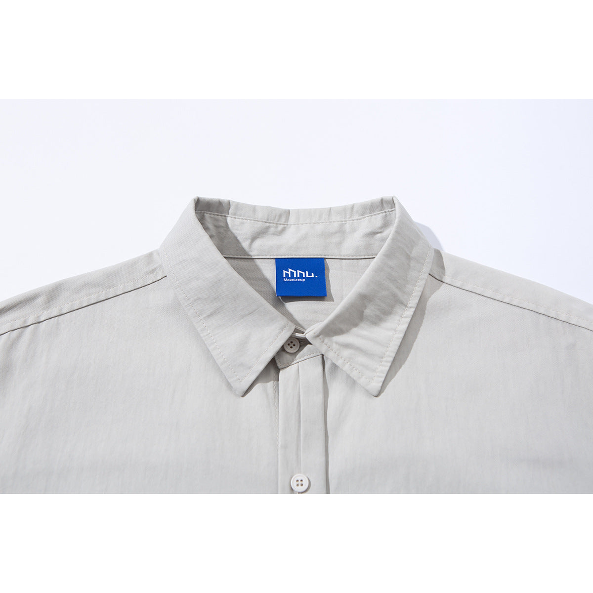 Close-up of a light gray button-up shirt collar and upper placket with a blue neck label.