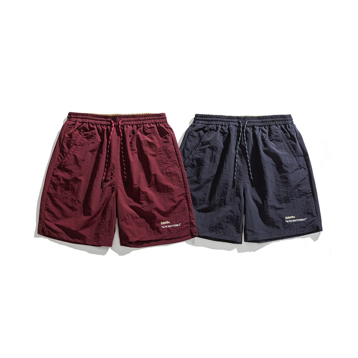 Front view of burgundy and dark navy shorts with elastic drawstring waists, side pockets and small embroidered lettering.