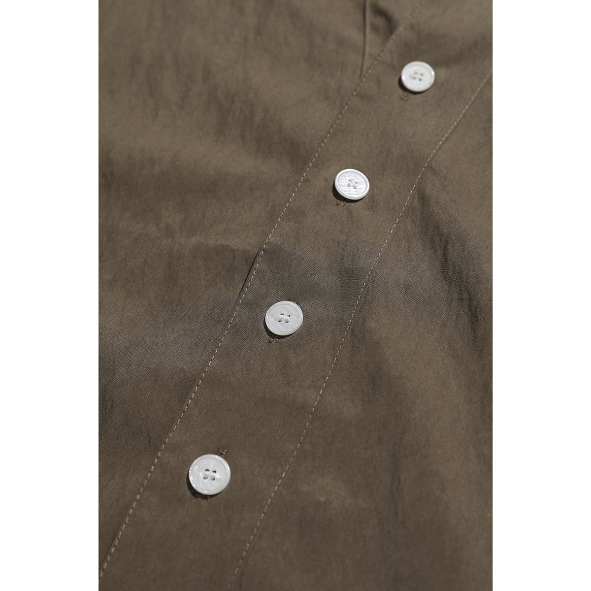 Close-up of the brown shirt's front placket with several white buttons and visible stitching.