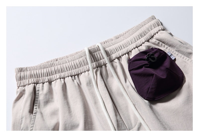 Close-up of light beige shorts with an elastic waistband, white drawcords, and a dark plum pocket.