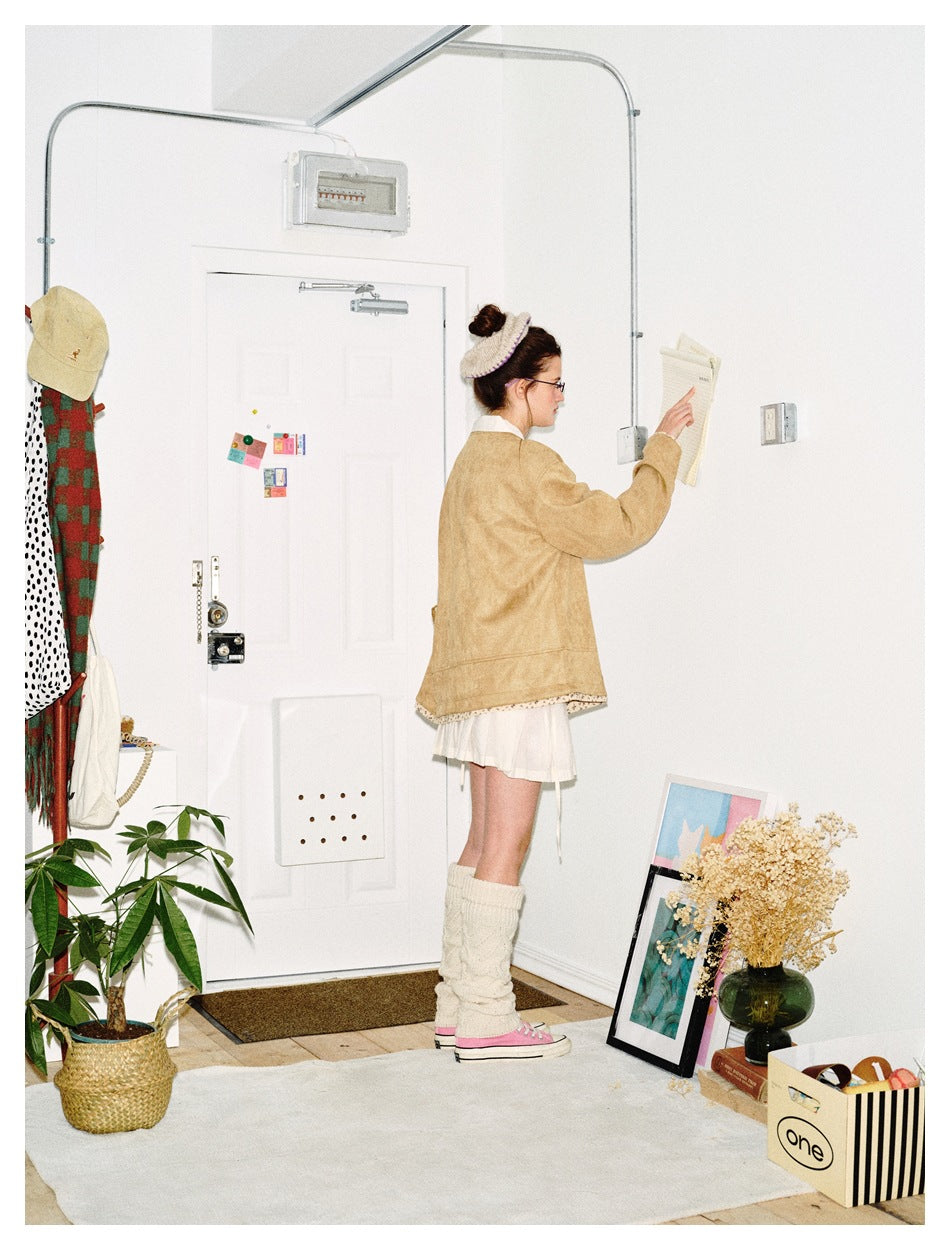 Side view of a model wearing a tan jacket with patterned hem trim over a short white skirt.