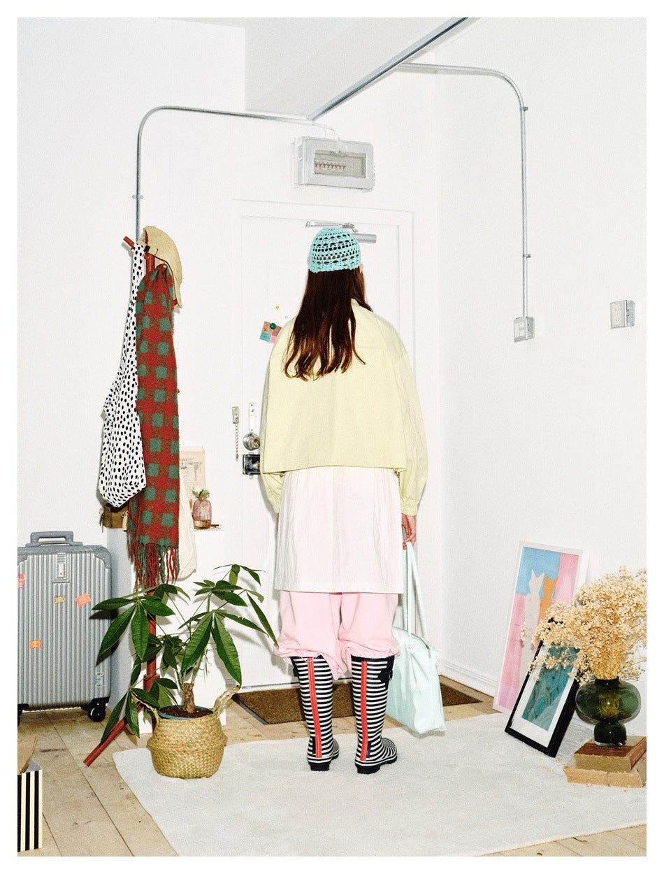 Rear view of a model wearing a pale yellow cropped jacket, white skirt, pink trousers and striped socks.