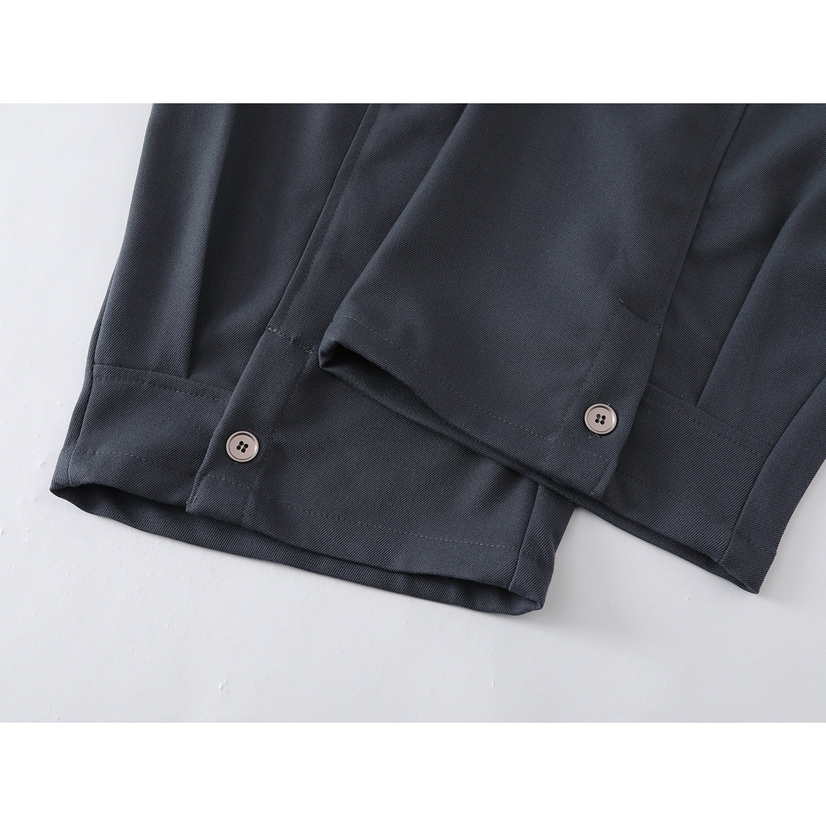 Close-up of charcoal trouser hems with button details and stitched cuffs.
