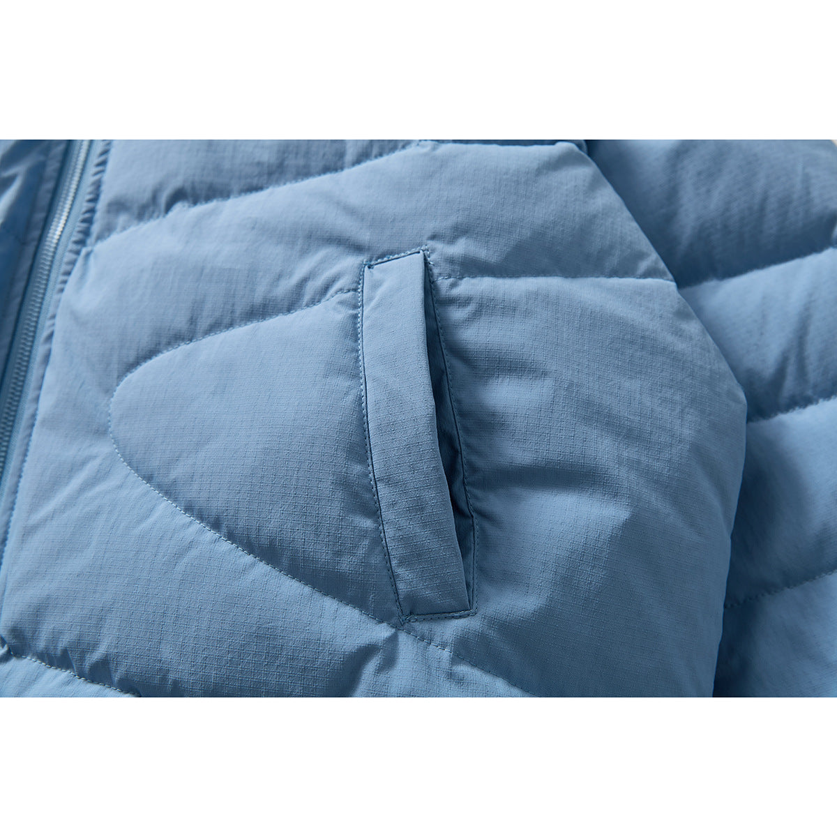 Close-up of a light blue quilted jacket pocket with a vertical opening.