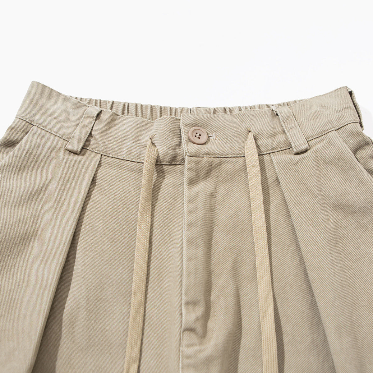 Close-up of beige trousers showing the buttoned waistband, belt loops, pleats and long drawstrings.