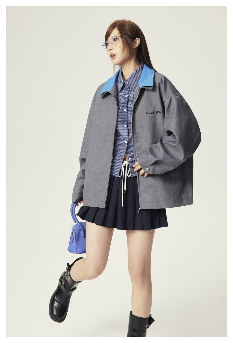 Three-quarter view of a model wearing an oversized gray jacket with a blue collar and a navy pleated skirt.