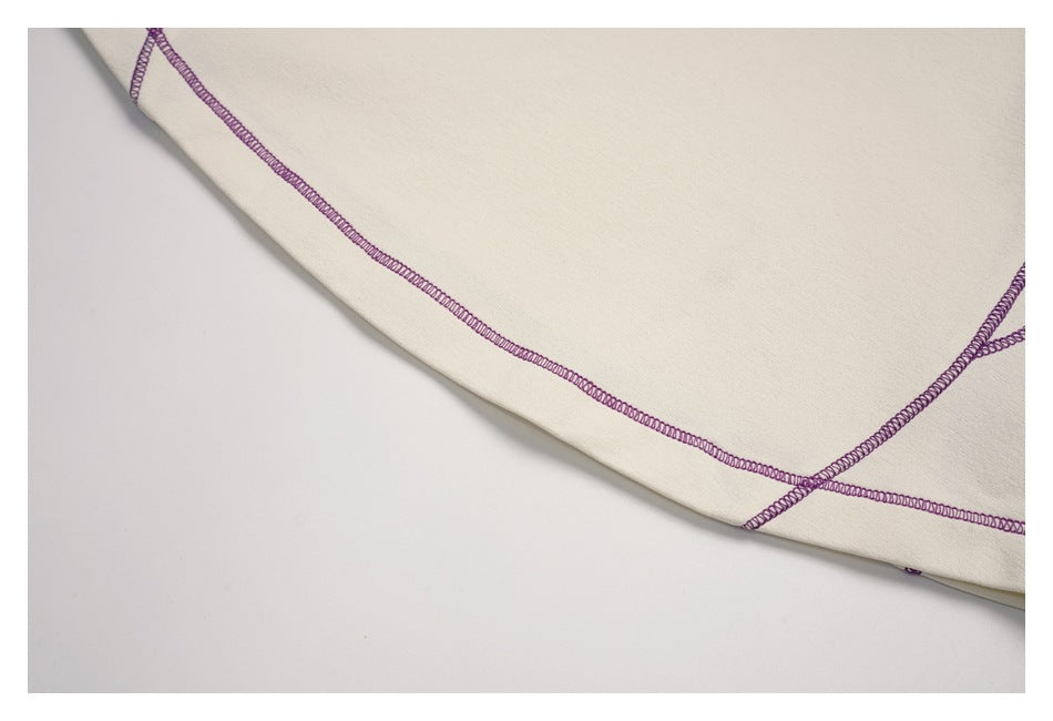 Close-up of a folded ivory garment edge with purple overlock stitching.