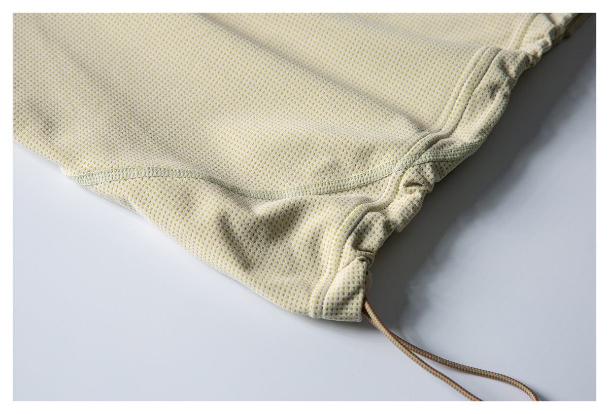 Close-up of cream dotted fabric, curved seam, gathered edge, and orange-and-teal drawcords.