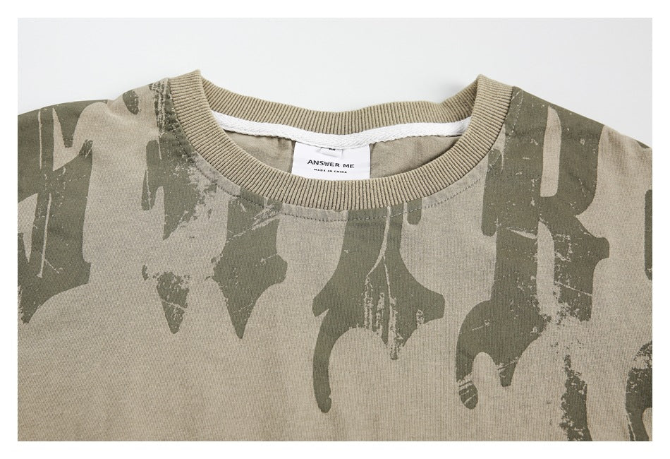 Upper front of a khaki T-shirt with an abstract dark olive print and ribbed crew neck.