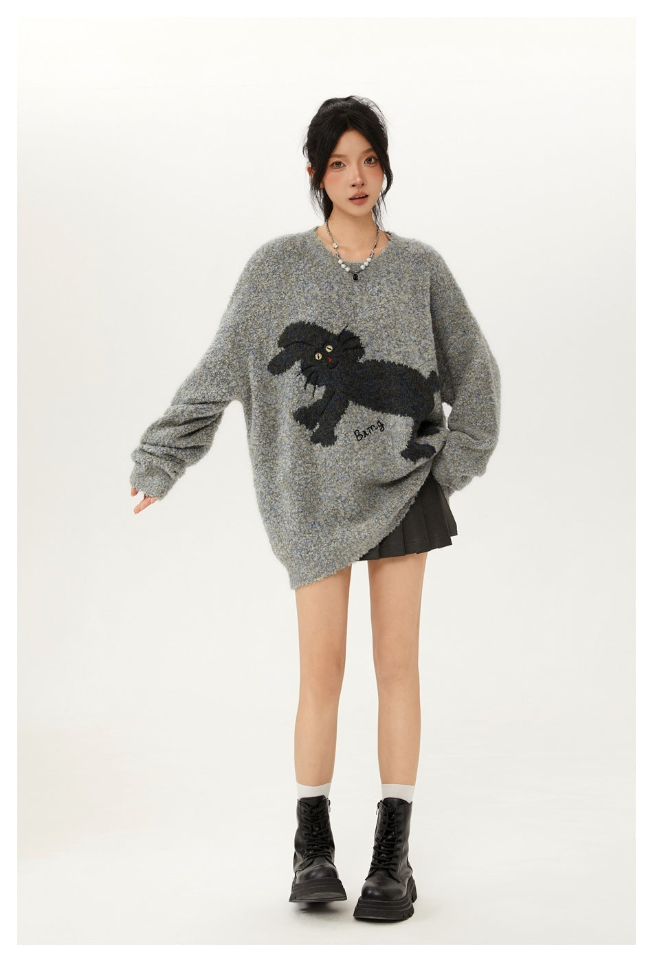 Model wearing an oversized gray knit sweater with a dark rabbit motif, pleated black mini skirt and black boots