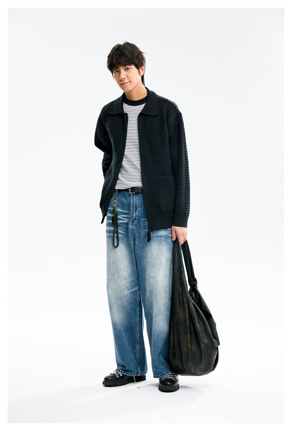 Model wearing a black textured knit jacket with a wide collar and patch pockets, styled with a striped shirt and loose jeans.