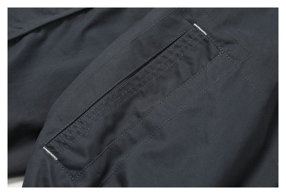 Close-up of a diagonal zip pocket with white bar-tack stitching on dark charcoal fabric.