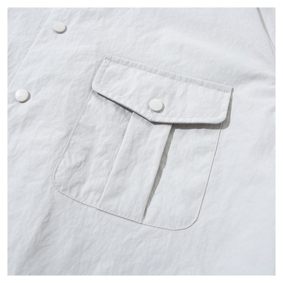 Close-up of a pale gray jacket's large flap pocket with a white snap button and visible stitching.