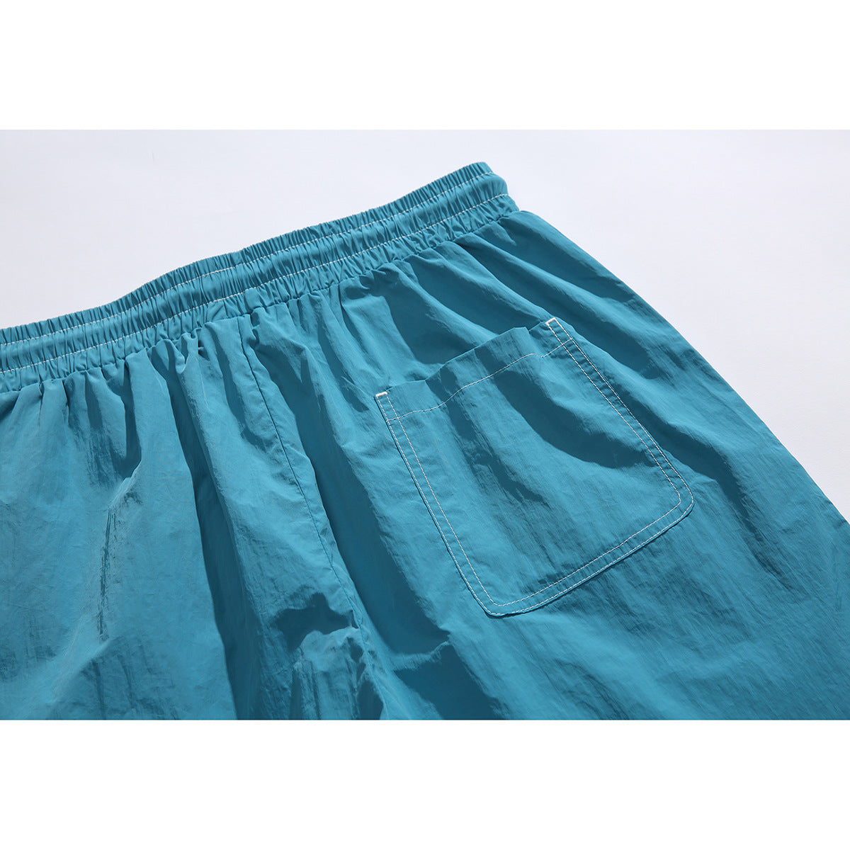 Close view of the back of teal shorts, showing the elastic waistband and a large stitched pocket.