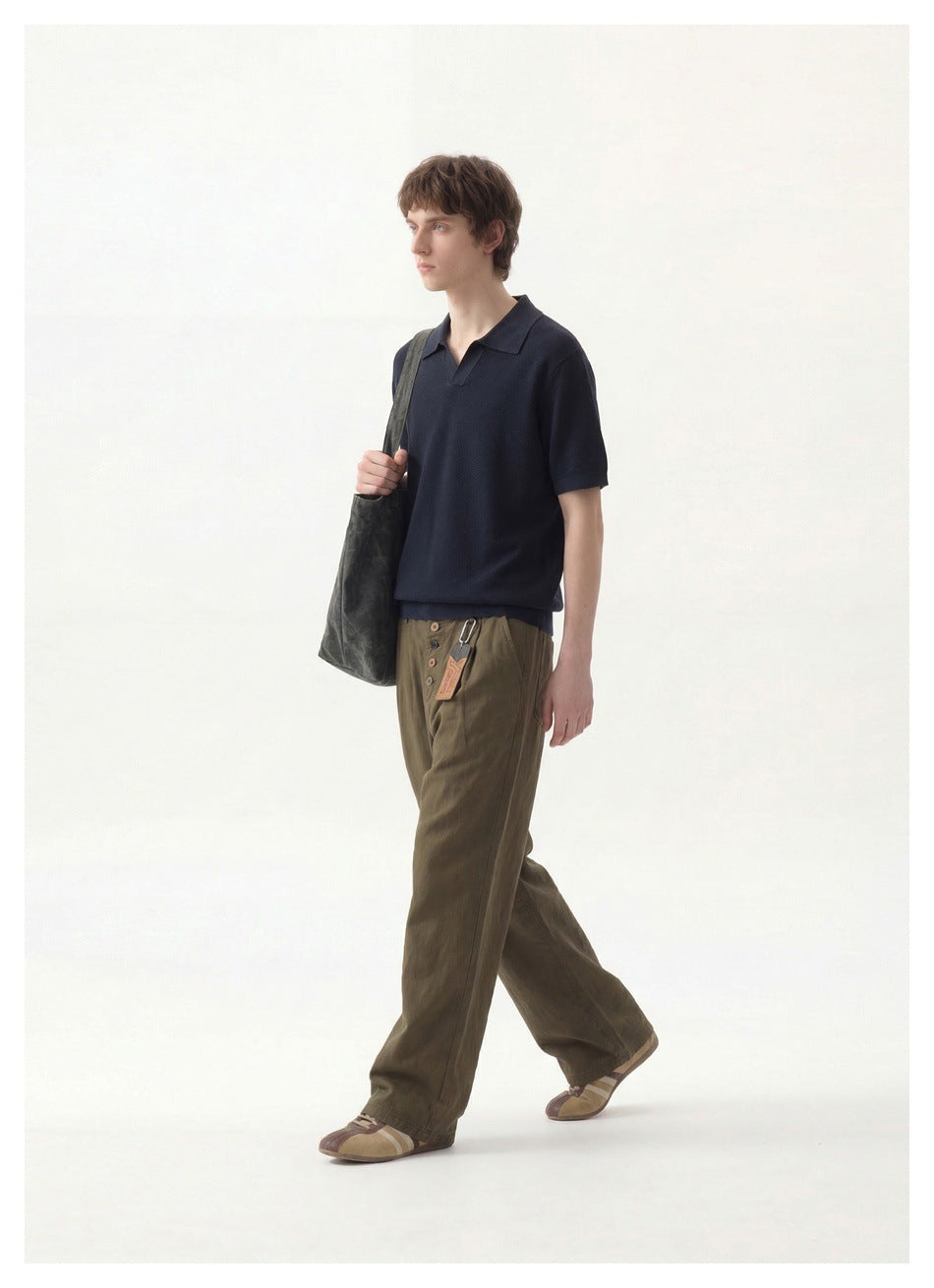 Model wearing a dark navy short-sleeve collared pullover with olive trousers, shown walking in a full-length view.